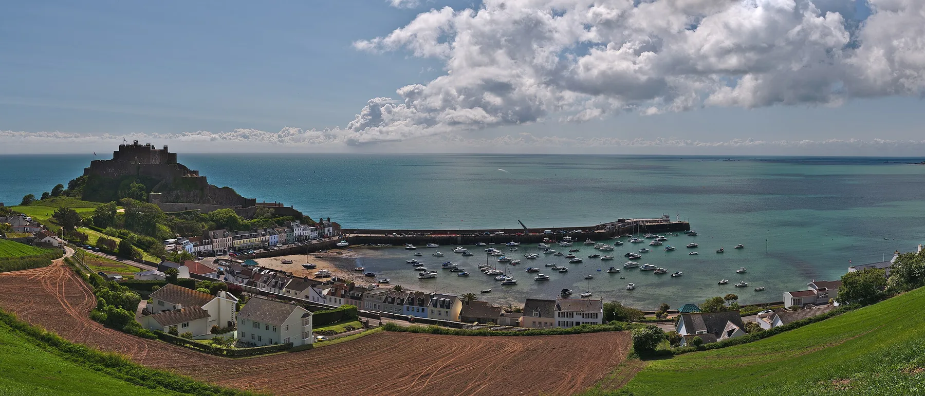 Mont Orgueil castle above Gorey harbour, with fishing boats moored on the sand and the east coast beyond